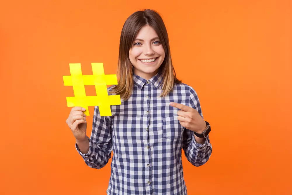 A imagem retrada uma mulher segurando um objeto em forma de hashtag (cerquilha #).
Fonte da imagem: Adobe Stock